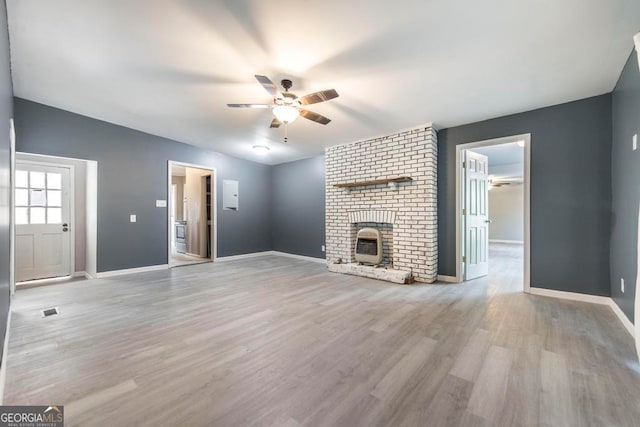 unfurnished living room featuring light wood-type flooring, a brick fireplace, and ceiling fan