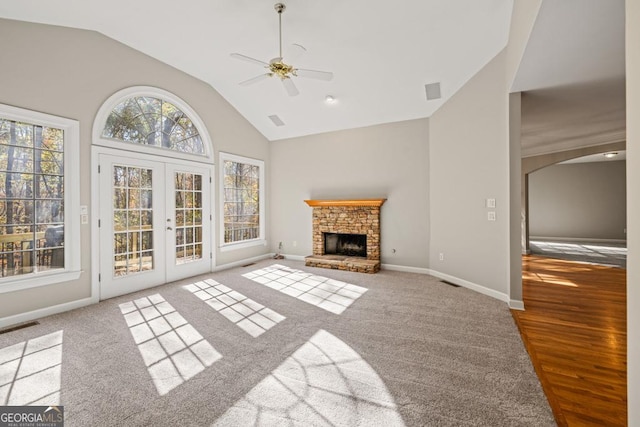 unfurnished living room featuring ceiling fan, french doors, a stone fireplace, lofted ceiling, and light wood-type flooring