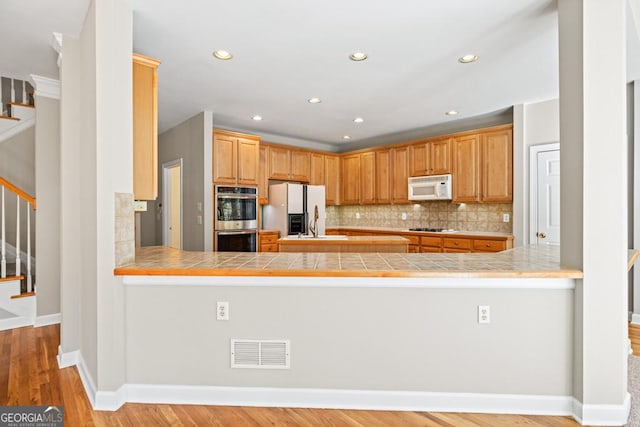 kitchen featuring tile counters, light wood-type flooring, white appliances, and kitchen peninsula