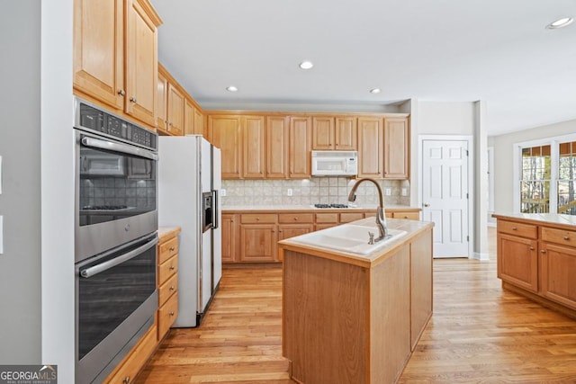 kitchen featuring light hardwood / wood-style flooring, an island with sink, white appliances, and light brown cabinets