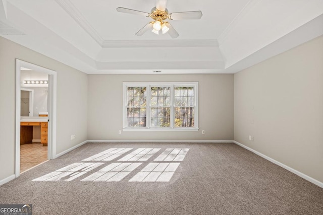 unfurnished bedroom with light carpet, ensuite bathroom, ceiling fan, ornamental molding, and a tray ceiling