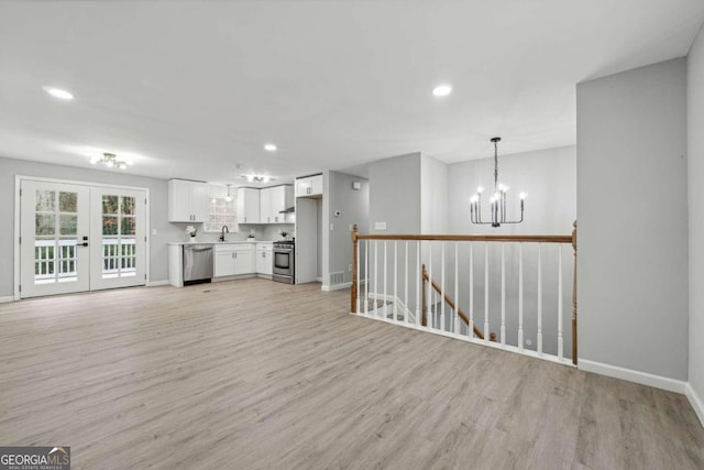 unfurnished living room featuring french doors, sink, a chandelier, and light hardwood / wood-style flooring