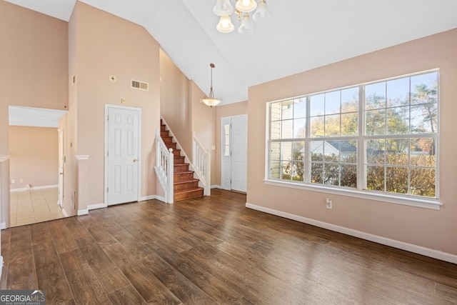 unfurnished living room with high vaulted ceiling, dark wood-type flooring, and an inviting chandelier