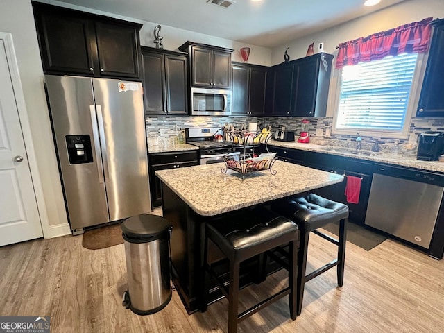 kitchen featuring stainless steel appliances, light hardwood / wood-style flooring, backsplash, a kitchen bar, and a kitchen island