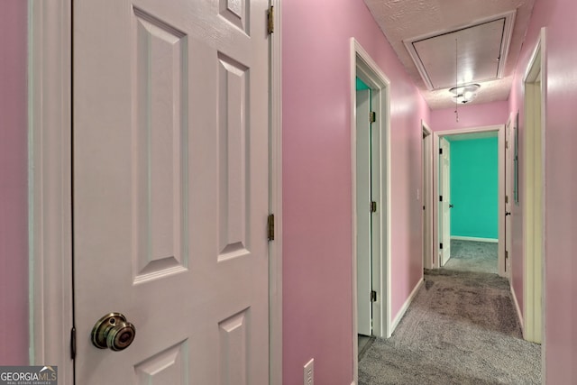 hall featuring attic access, carpet floors, and baseboards
