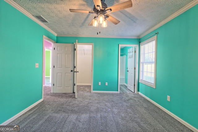 unfurnished bedroom featuring carpet flooring, ceiling fan, a spacious closet, a textured ceiling, and ornamental molding