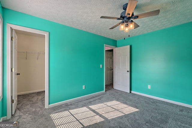 unfurnished bedroom with a spacious closet, ceiling fan, a textured ceiling, a closet, and carpet