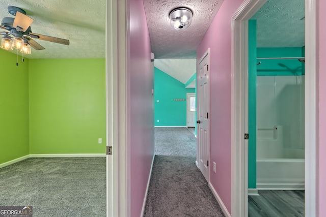 hallway with baseboards, a textured ceiling, carpet, and vaulted ceiling