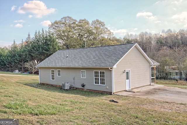 exterior space featuring a shingled roof, cooling unit, and a lawn