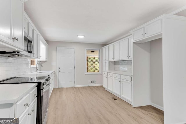 kitchen featuring backsplash, white cabinetry, light hardwood / wood-style flooring, and appliances with stainless steel finishes