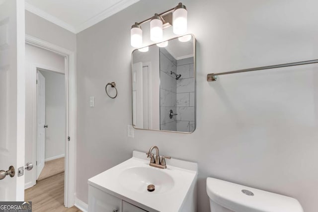 bathroom featuring ornamental molding, vanity, tiled shower, wood-type flooring, and toilet