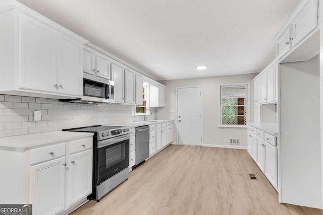 kitchen featuring light hardwood / wood-style floors, white cabinetry, backsplash, and appliances with stainless steel finishes