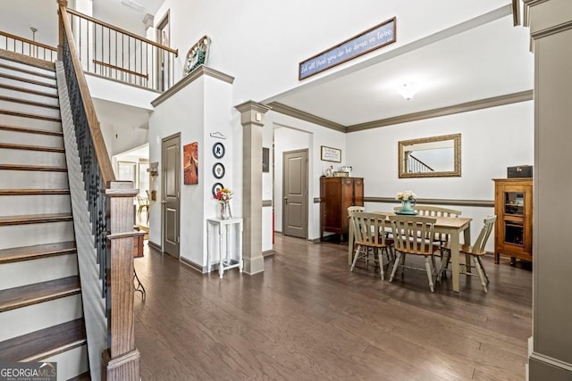 dining space with ornamental molding, a towering ceiling, decorative columns, and dark wood-type flooring