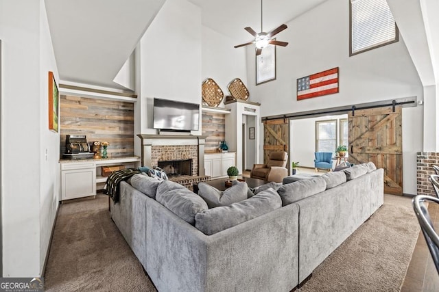 carpeted living room with wooden walls, a brick fireplace, ceiling fan, a barn door, and a towering ceiling