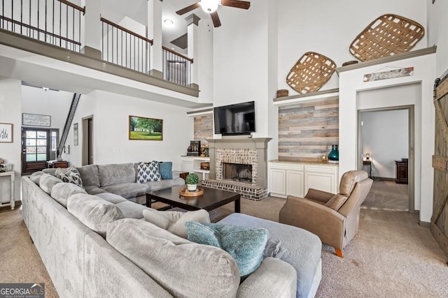 living room with ceiling fan, a fireplace, a towering ceiling, and light colored carpet