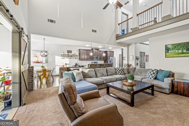 living room featuring light carpet, a high ceiling, a barn door, and ceiling fan