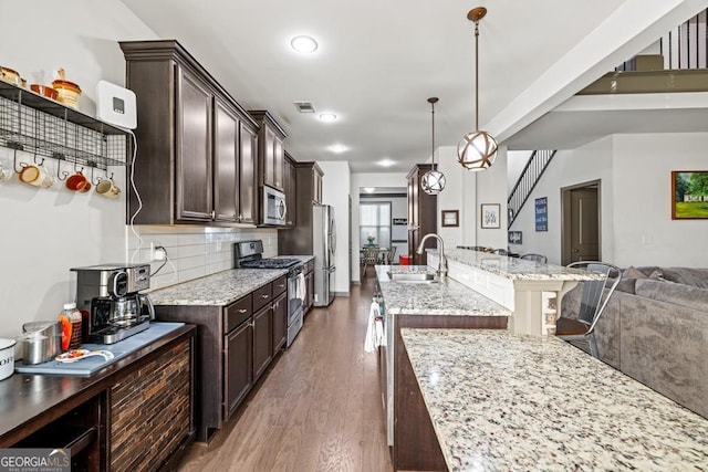 kitchen with light stone countertops, sink, hanging light fixtures, dark hardwood / wood-style flooring, and appliances with stainless steel finishes