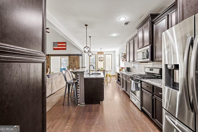 kitchen with a breakfast bar, a center island with sink, hanging light fixtures, dark hardwood / wood-style floors, and stainless steel appliances