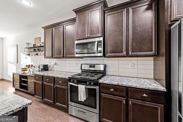 kitchen with light stone countertops, stainless steel appliances, tasteful backsplash, light hardwood / wood-style flooring, and dark brown cabinets