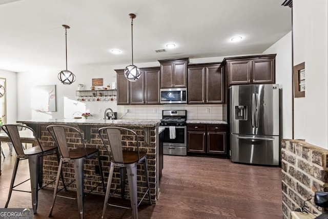 kitchen featuring a breakfast bar area, dark wood-type flooring, decorative light fixtures, and appliances with stainless steel finishes