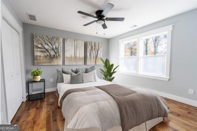 bedroom with baseboards, visible vents, dark wood finished floors, and a closet