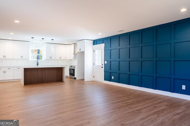 unfurnished living room featuring light wood-type flooring, a decorative wall, a sink, and recessed lighting