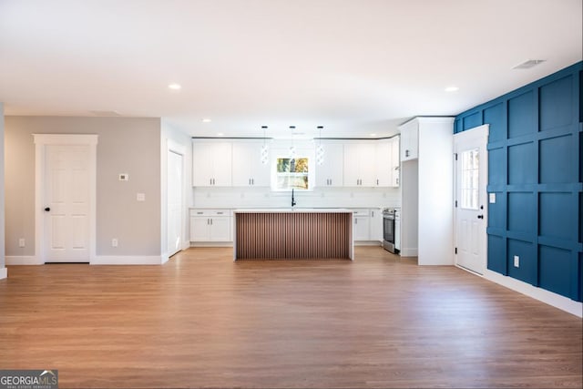 kitchen with a kitchen island, white cabinetry, light countertops, hanging light fixtures, and stainless steel range