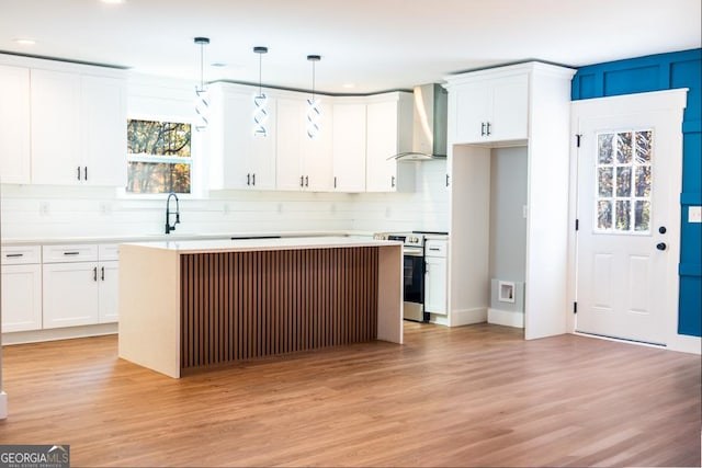 kitchen featuring hanging light fixtures, wall chimney exhaust hood, light countertops, and electric stove