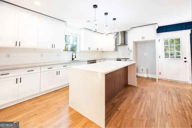 kitchen featuring a sink, a kitchen island, hanging light fixtures, light countertops, and wall chimney exhaust hood