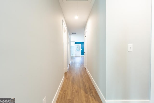 corridor with attic access, visible vents, light wood-style flooring, and baseboards