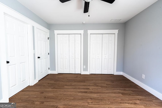 unfurnished bedroom with multiple closets, a ceiling fan, baseboards, and dark wood-style floors