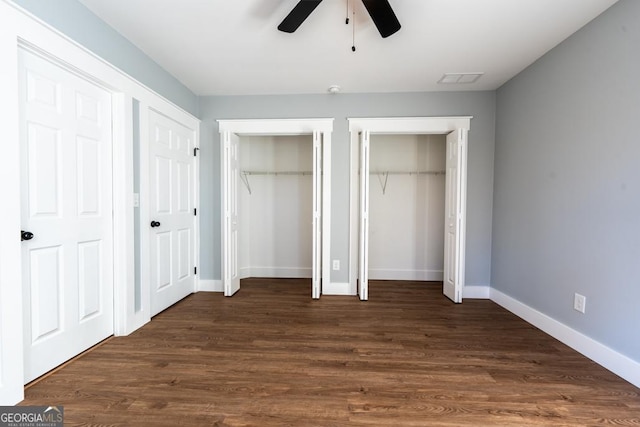 unfurnished bedroom with ceiling fan, baseboards, dark wood-style flooring, and two closets