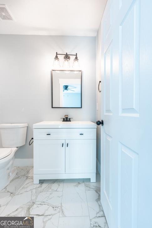 half bath with marble finish floor, visible vents, vanity, and toilet