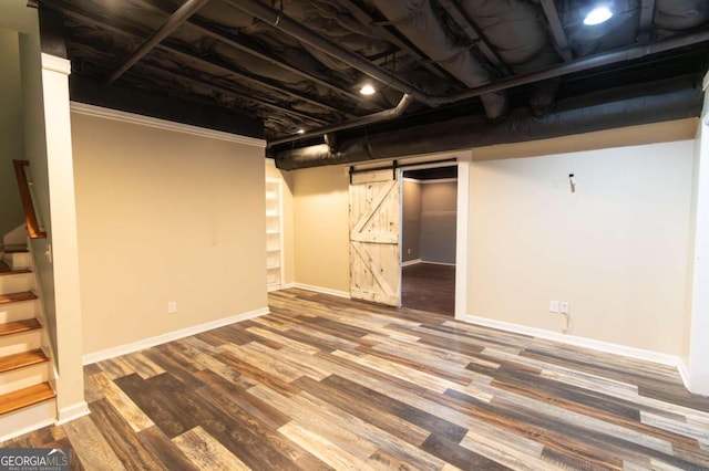 basement with a barn door, wood-type flooring, and crown molding