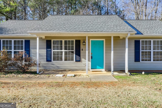 single story home with covered porch, roof with shingles, and a front lawn