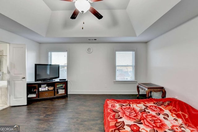 bedroom with a raised ceiling, connected bathroom, ceiling fan, and dark hardwood / wood-style flooring