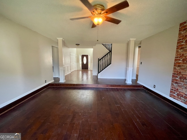 spare room with a textured ceiling, dark hardwood / wood-style floors, ornate columns, and ceiling fan