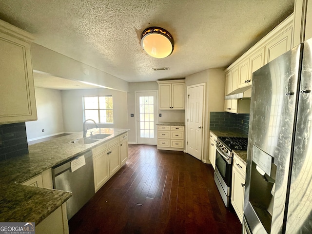 kitchen with sink, dark hardwood / wood-style flooring, backsplash, dark stone countertops, and appliances with stainless steel finishes