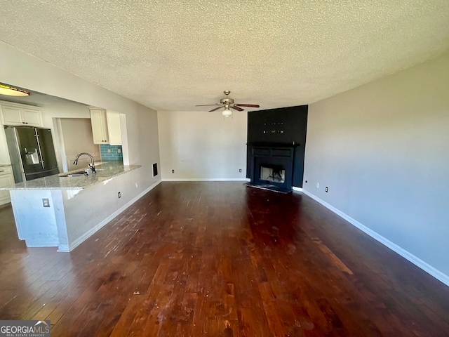 unfurnished living room with a textured ceiling, dark hardwood / wood-style floors, ceiling fan, and sink