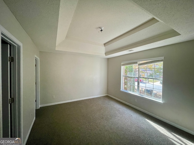 empty room with dark carpet, a textured ceiling, and a raised ceiling