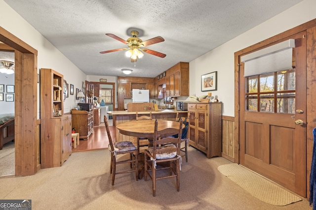 carpeted dining area featuring a textured ceiling, ceiling fan, and wood walls