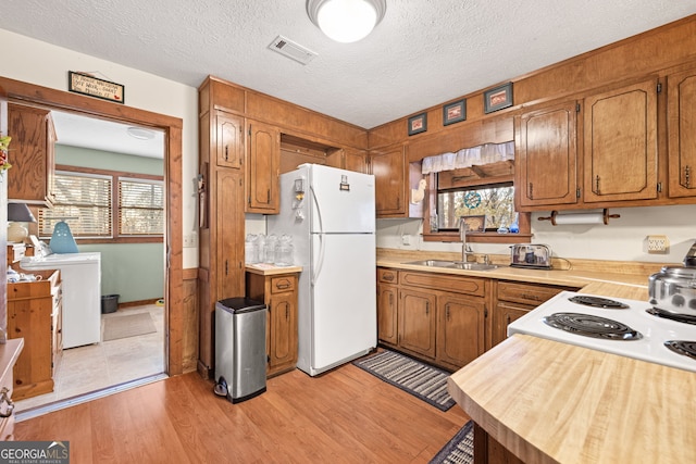 kitchen with a textured ceiling, white appliances, sink, and light hardwood / wood-style flooring