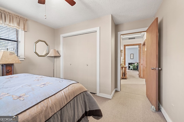 bedroom featuring ceiling fan, light colored carpet, a textured ceiling, and a closet