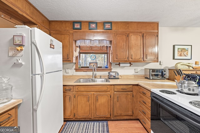 kitchen with a textured ceiling, light wood-type flooring, white appliances, and sink