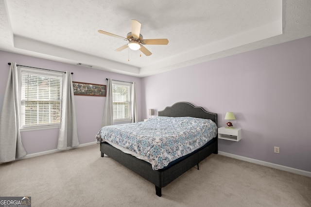 bedroom featuring a textured ceiling, ceiling fan, a raised ceiling, and light carpet