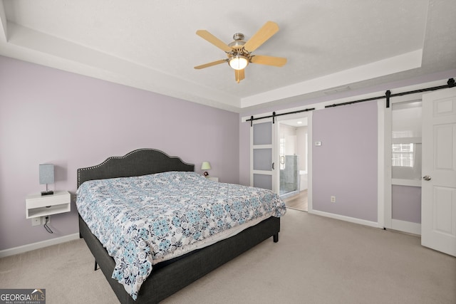 carpeted bedroom with a tray ceiling, a barn door, ensuite bathroom, and ceiling fan