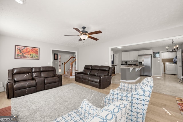 living room with ceiling fan with notable chandelier, sink, a textured ceiling, light hardwood / wood-style floors, and washer / dryer