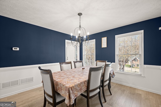 dining room featuring light hardwood / wood-style floors, a textured ceiling, and an inviting chandelier