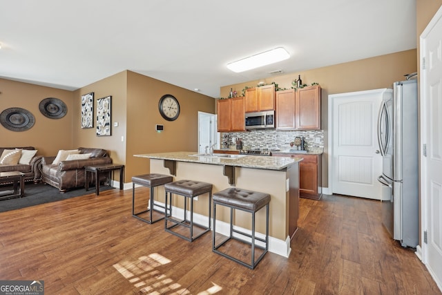 kitchen with a kitchen bar, stainless steel appliances, a kitchen island with sink, and dark hardwood / wood-style floors