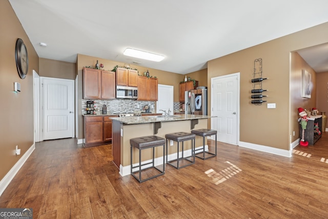 kitchen with light stone counters, a breakfast bar area, a kitchen island with sink, appliances with stainless steel finishes, and hardwood / wood-style flooring